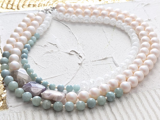 Three-strand layered necklace with pearls, quartz, and purplish earth-tone gemstones.
