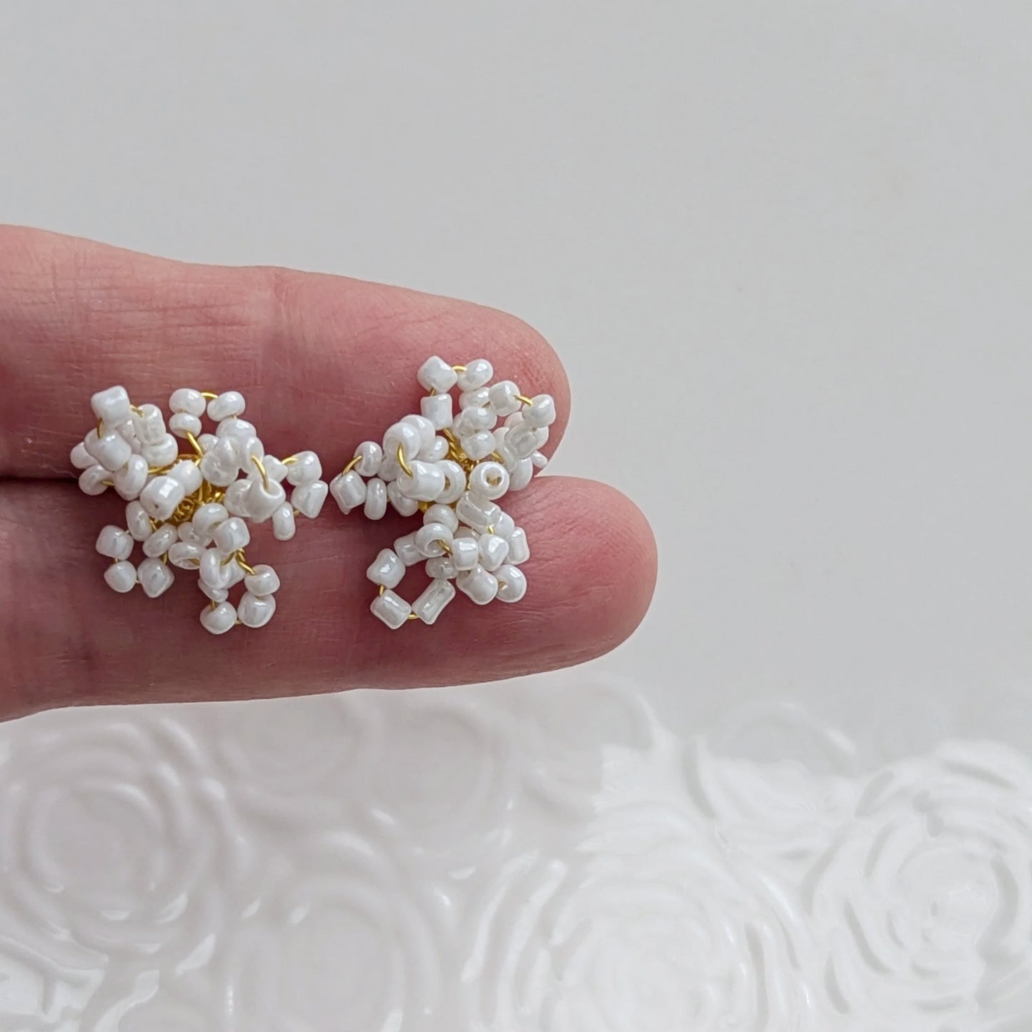 Delicate floral earrings crafted from tiny white beads and gold wire for weddings.