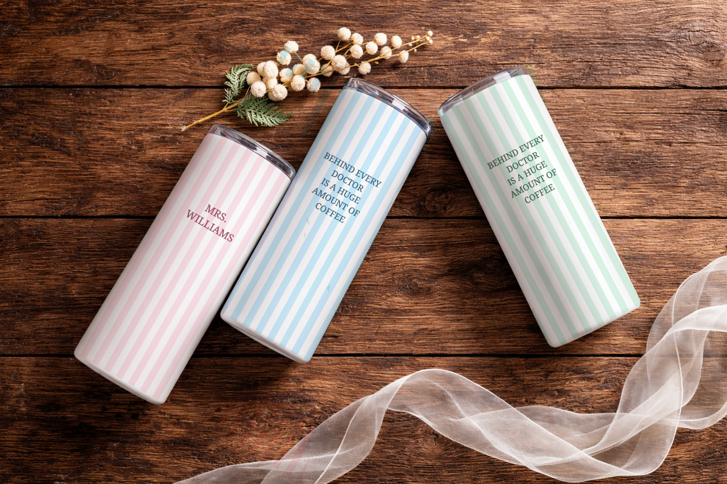 Three insulated tumblers with personalized text on a wooden surface with decorative elements.