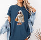 Crocheted Boojee ghost figure is on the midnight blue Comfort Colors shirt. The model has long blonde hair, her jean jacket fell down drom her arms to show her ghost printed shirt. She looks beautiful, sport, eye catching, cute and so happy.