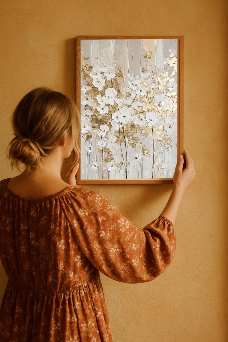 The textured wall art has a golden white floral oil painting with a golden foil effect and the bohemian girl is hanging on the terracota colored wall.