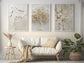 Textured 3 wall art design hanging on a beige wall. The room has white loveseat with some plants. One of the frame is textured minimal brushstrokes, The wall art in the middle is with white and gold color elegant tree, the wall art on the right side has golden white floral oil painting with golden foil effect.