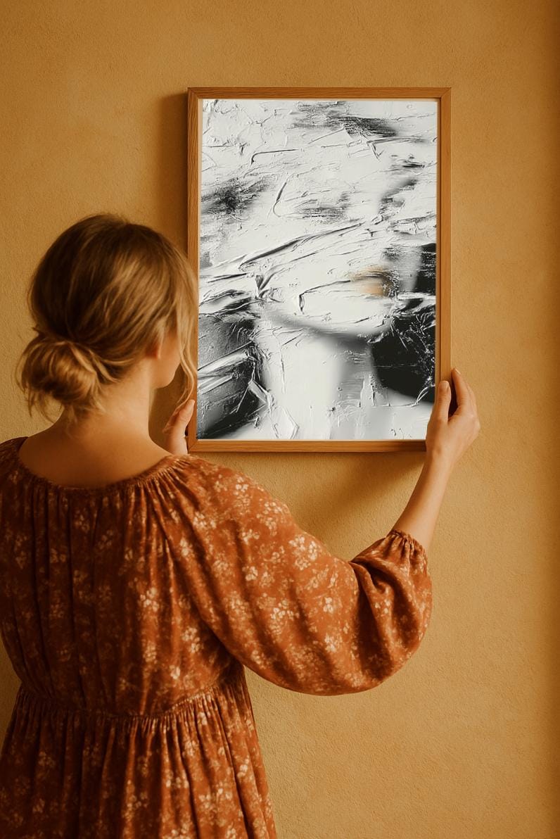 Woman in floral brown dress hanging neutral textured abstract face wabi sabi artwork on beige wall.