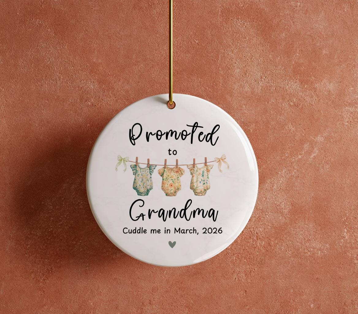 May include: A white ceramic ornament with the text "Promoted to Grandma" in black script. Below the text are three baby onesies hanging on a clothesline. The ornament also includes the text "Cuddle me in March, 2026" and a small heart.