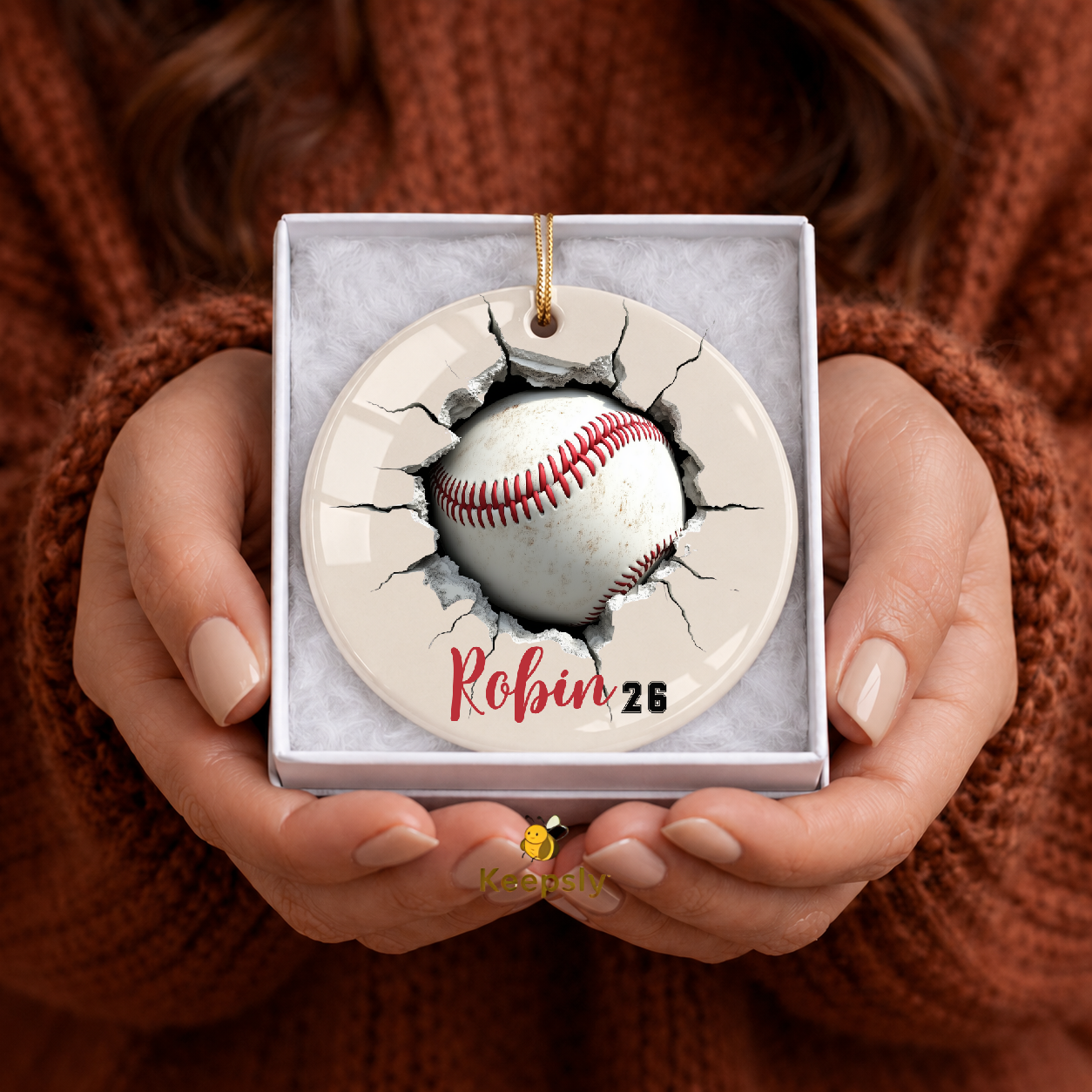 Decorative baseball ornament with a 3D cracked wall baseball design held in hands against a brown textured background