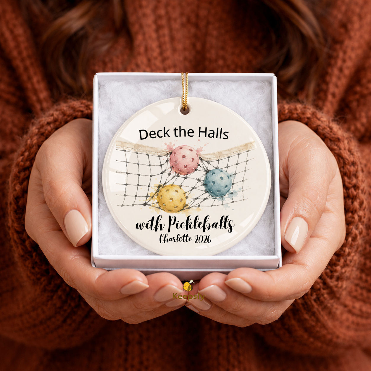 Person holding a decorative ornament with colorful pickleballs and text in a box.